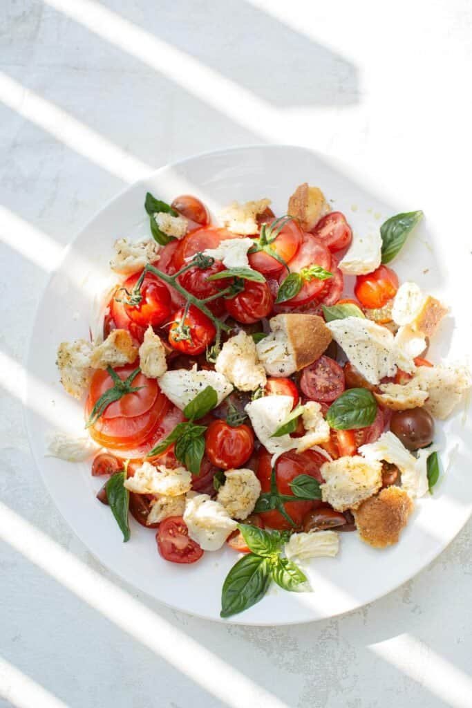 Fresh cherry tomato salad with basil, mozzarella, and croutons on a white plate.