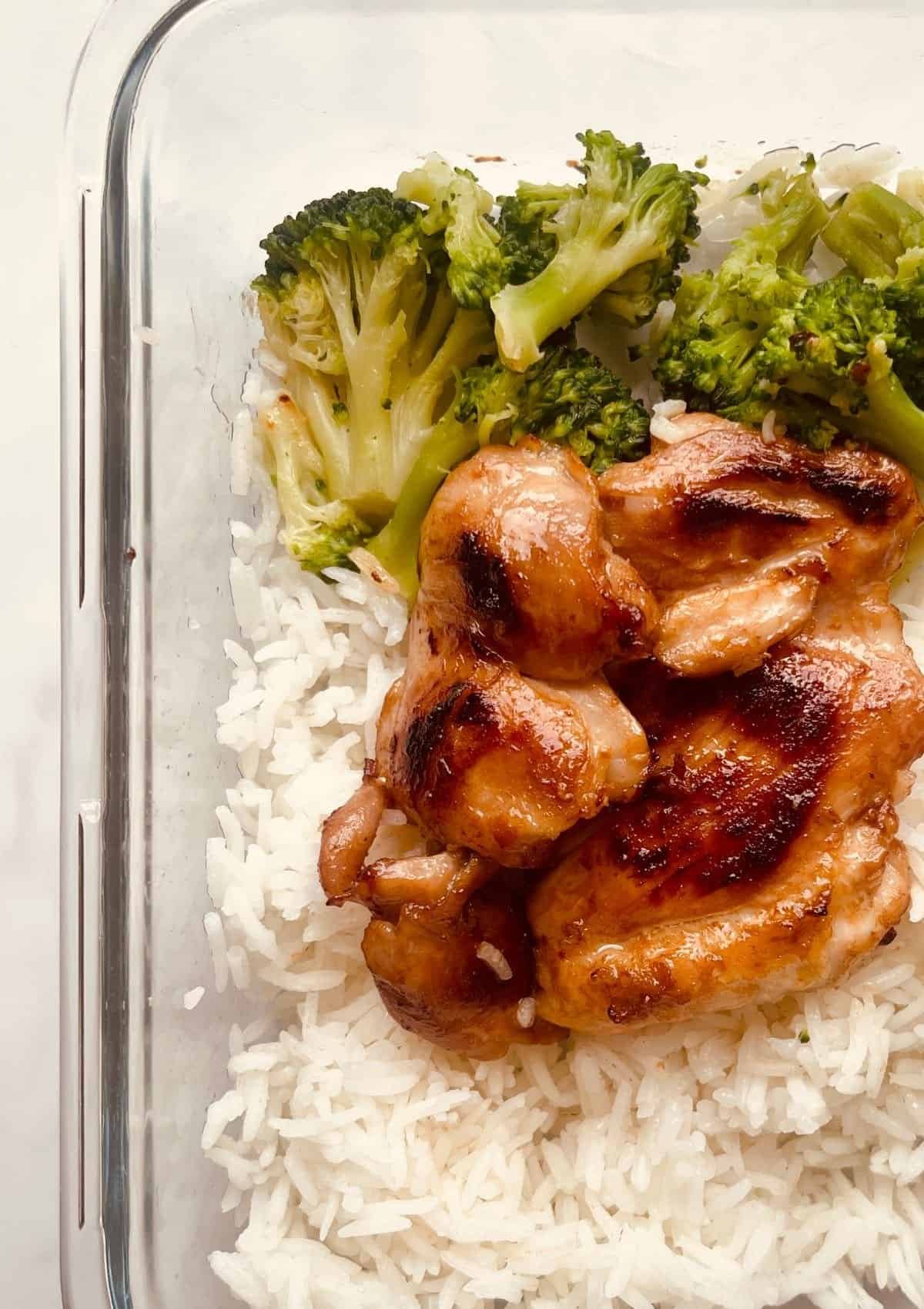 Juicy honey garlic chicken with steamed broccoli and white rice in a glass meal prep container.