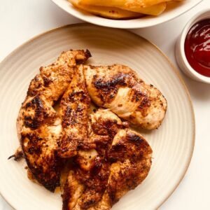 Grilled lemon garlic chicken with crispy fries and ketchup on a white plate.
