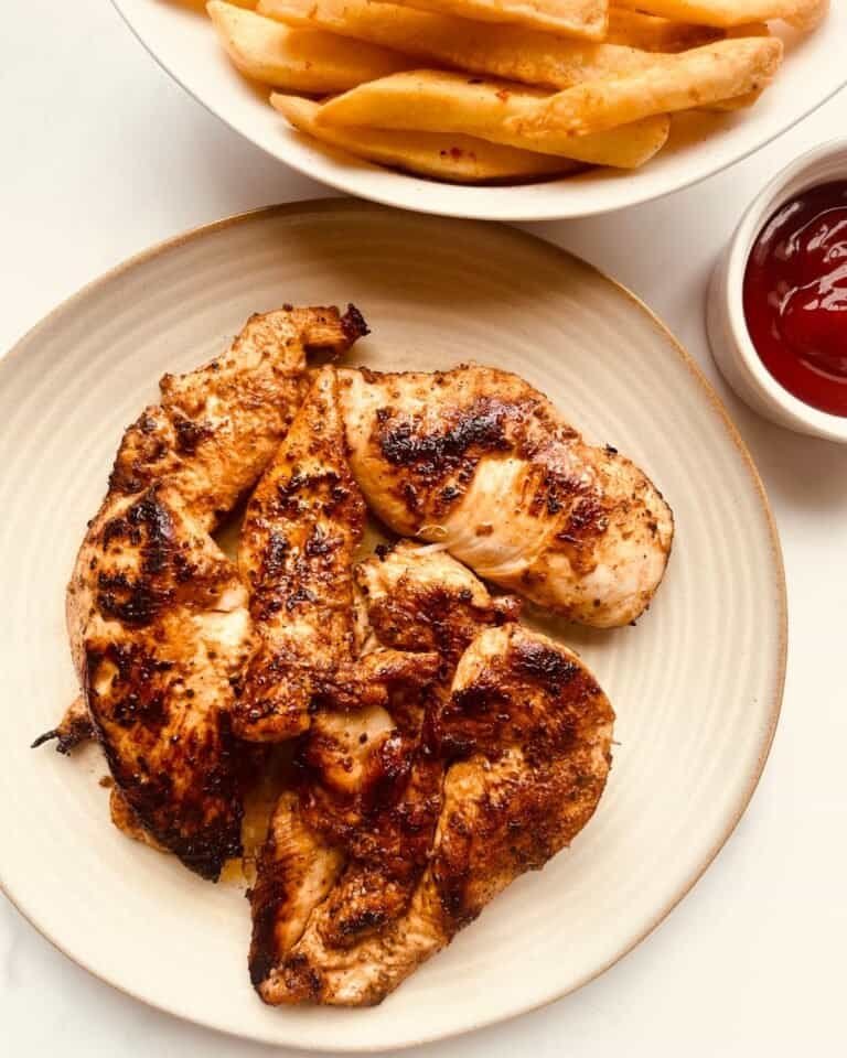 Grilled lemon garlic chicken with crispy fries and ketchup on a white plate.