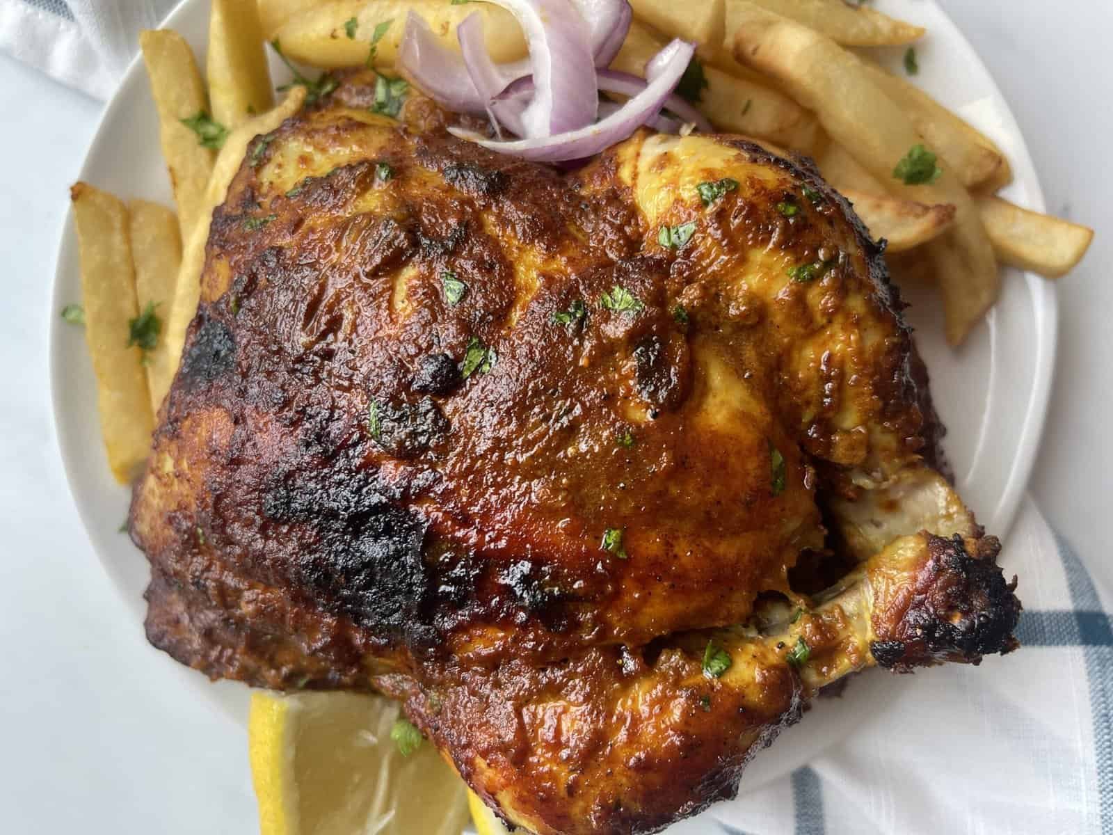 Grilled Lebanese chicken with crispy fries and fresh onion slices on a white plate.