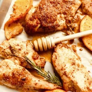 Grilled honey orange Dijon chicken with roasted potatoes and fresh herbs on a baking sheet.