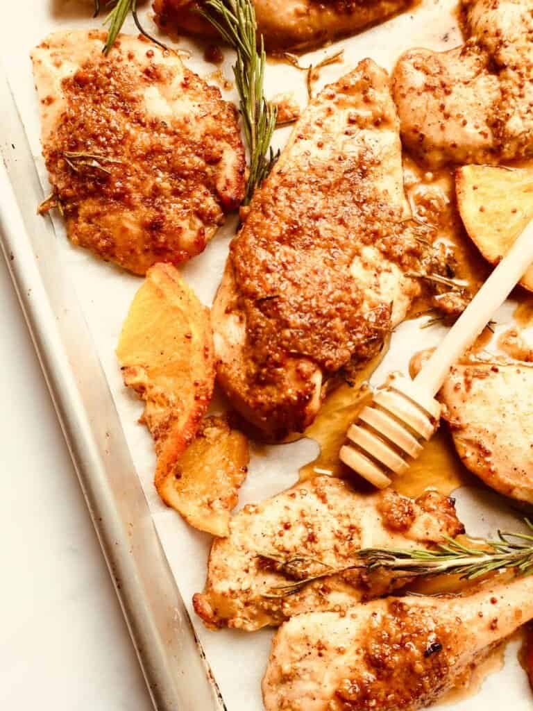 Juicy honey orange Dijon chicken thighs on a sheet pan with roasted potatoes and fresh rosemary.