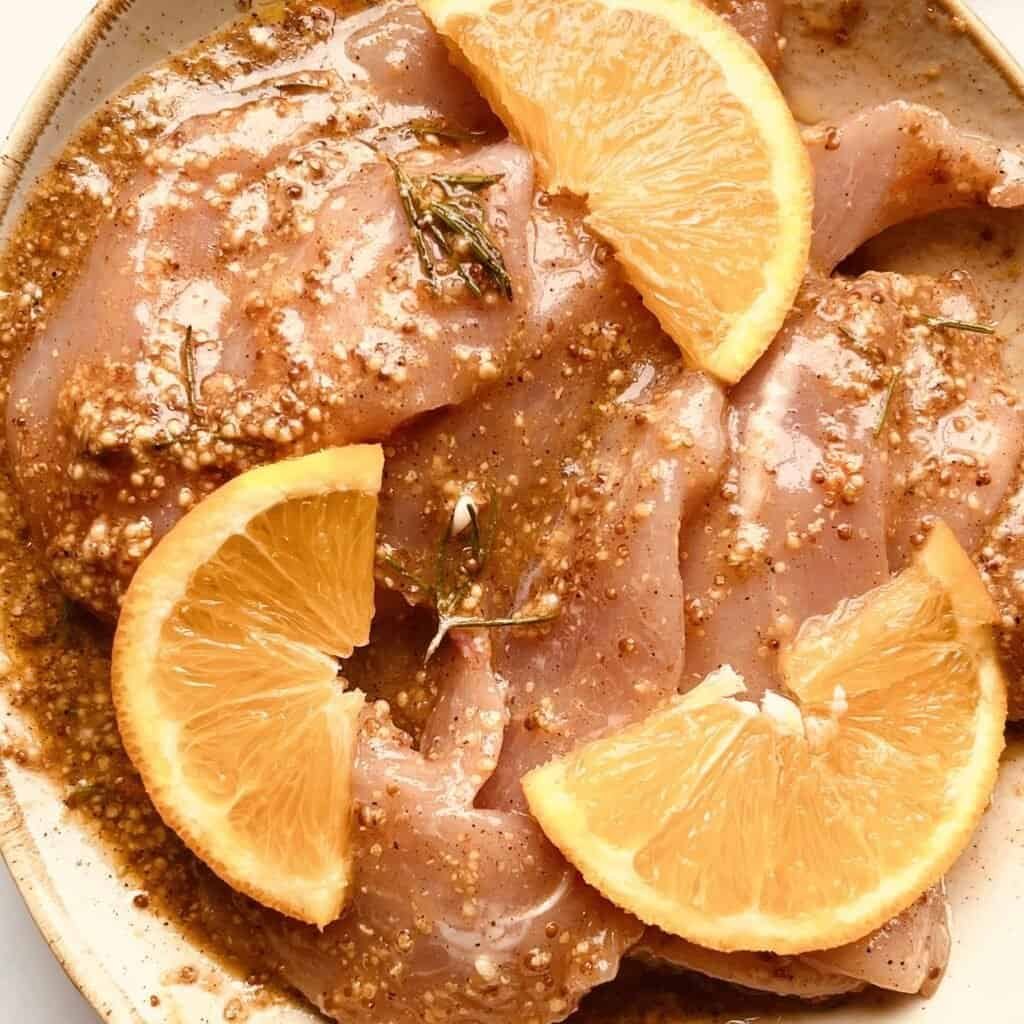 Juicy orange-glazed chicken thighs with herbs on a white plate.