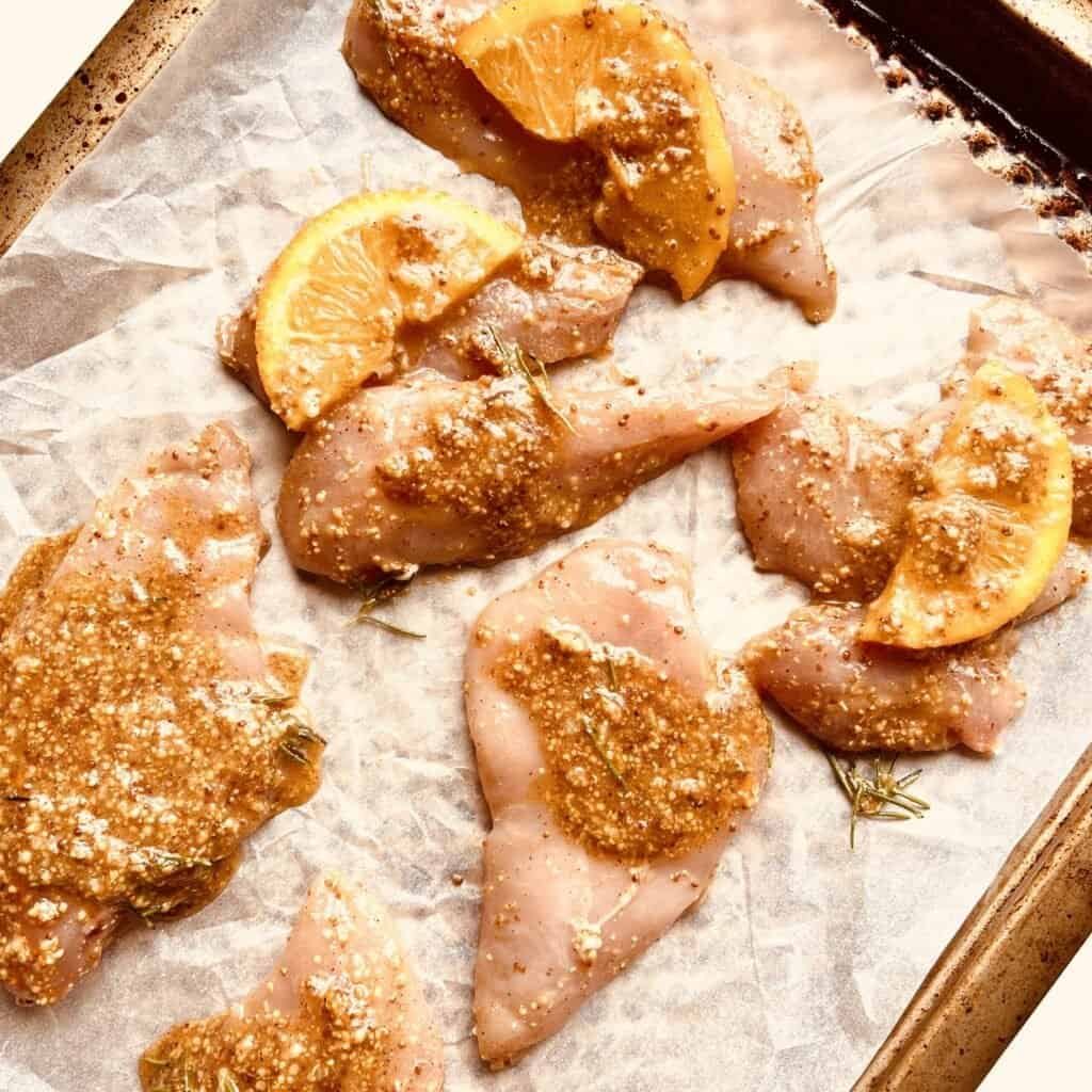 Grilled chicken thighs with lemon slices and seasoning on parchment paper.