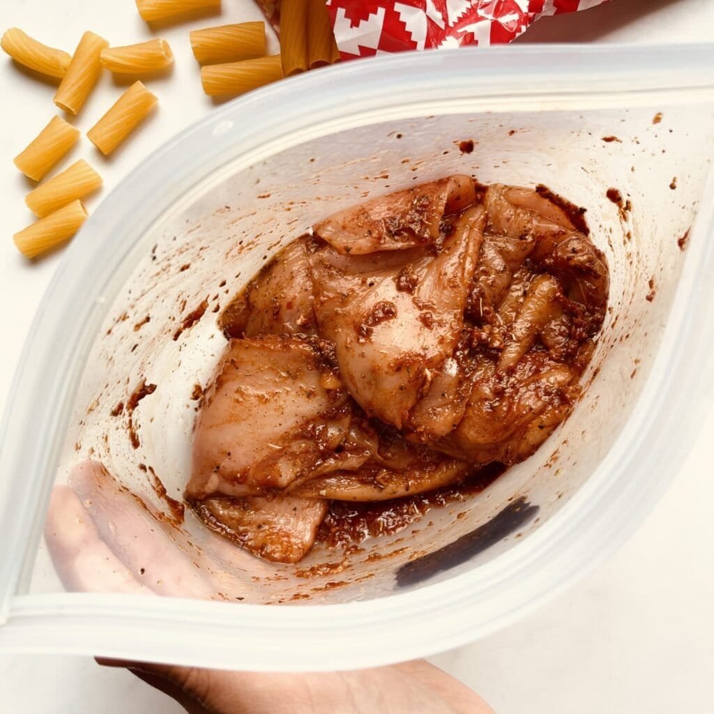 Grilled chicken marinated in herbs and spices in a clear container for Italian pasta recipe.