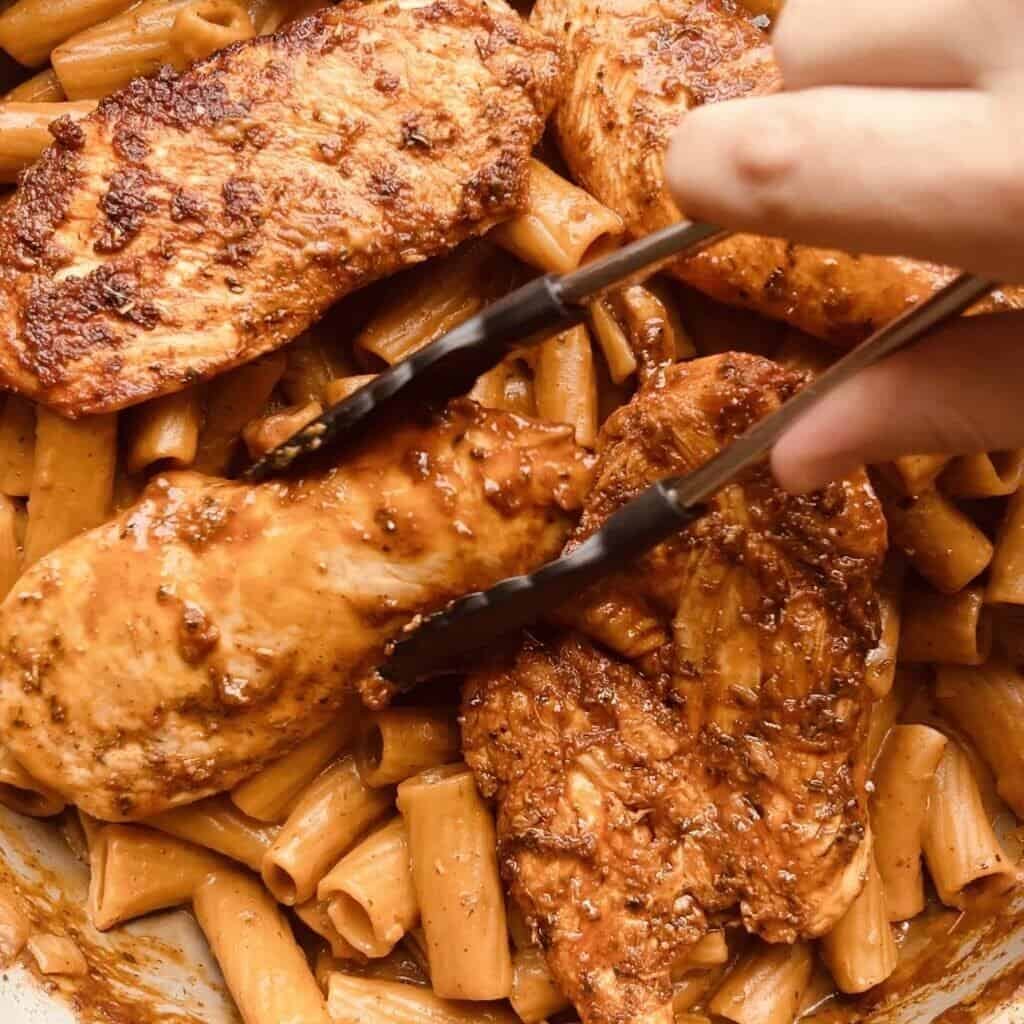 Juicy Italian chicken breasts with pasta and rich herb marinade in a skillet.