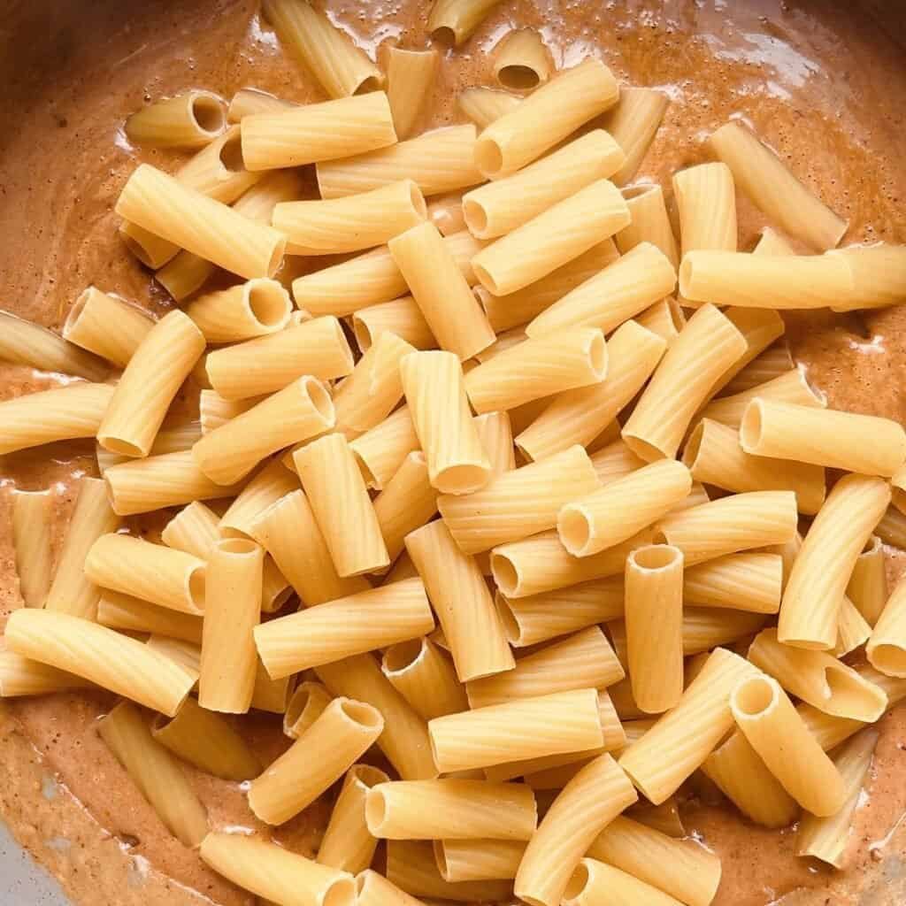 Creamy Italian chicken pasta with uncooked rigatoni and herb marinade in a skillet.