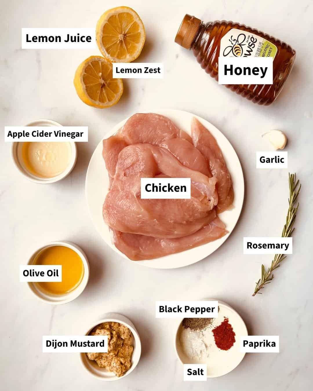 Juicy chicken breasts with honey mustard marinade ingredients on a white surface.