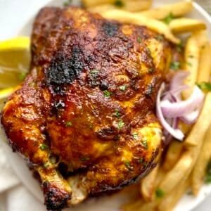 Grilled Lebanese chicken with crispy fries and fresh herbs on a white plate.