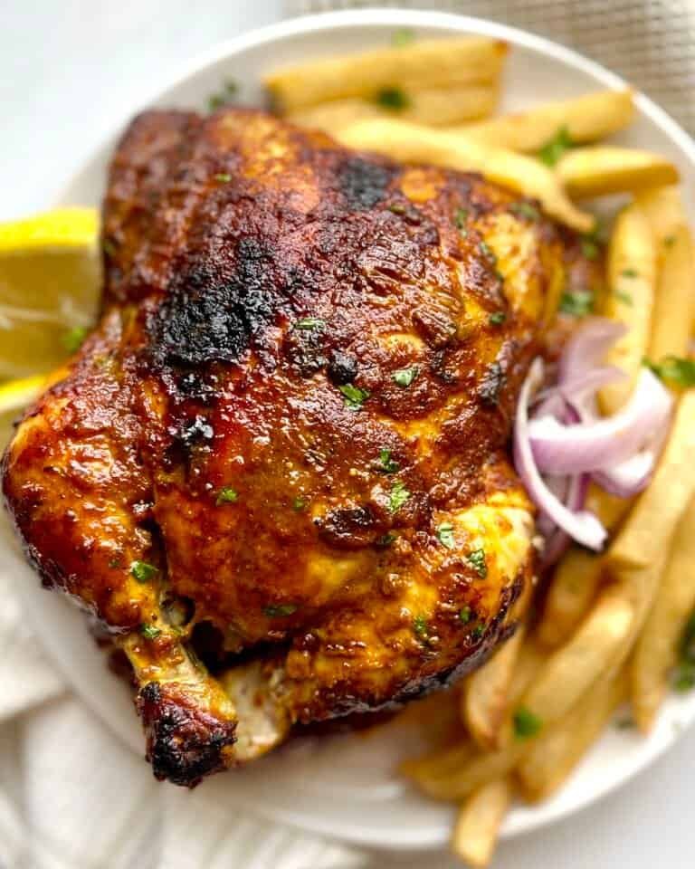 Grilled Lebanese chicken with crispy fries and fresh herbs on a white plate.