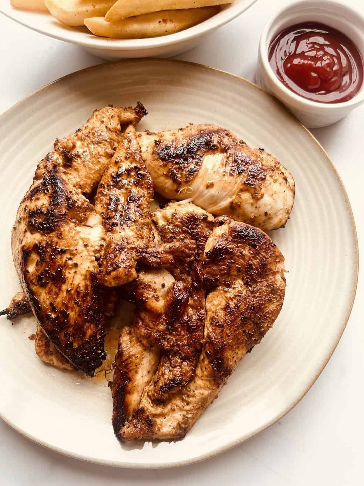 Juicy lemon garlic chicken thighs with crispy skin on a beige plate, served with ketchup in a small.
