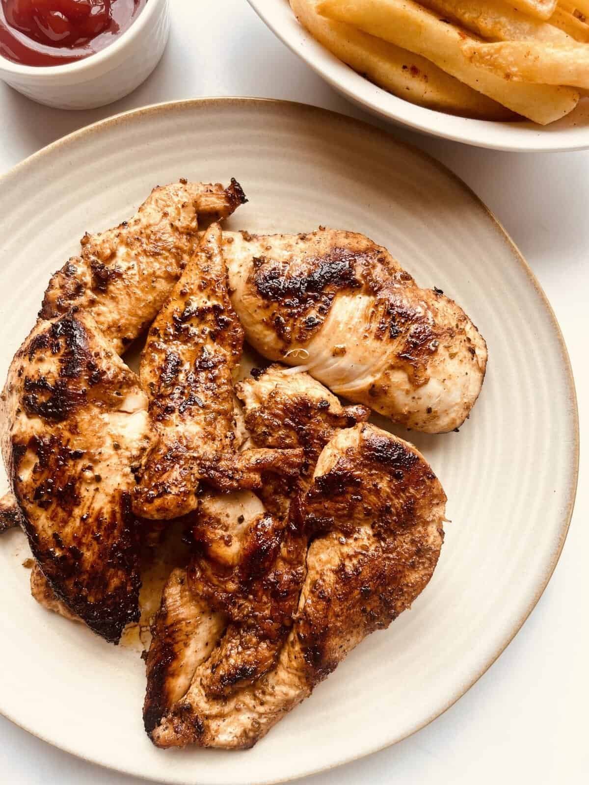 Grilled lemon garlic chicken thighs on a beige plate with side of fries and ketchup.