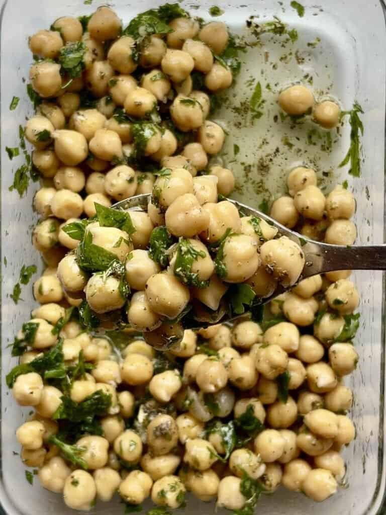 Soft, marinated chickpeas with herbs in a glass dish, ready to serve.