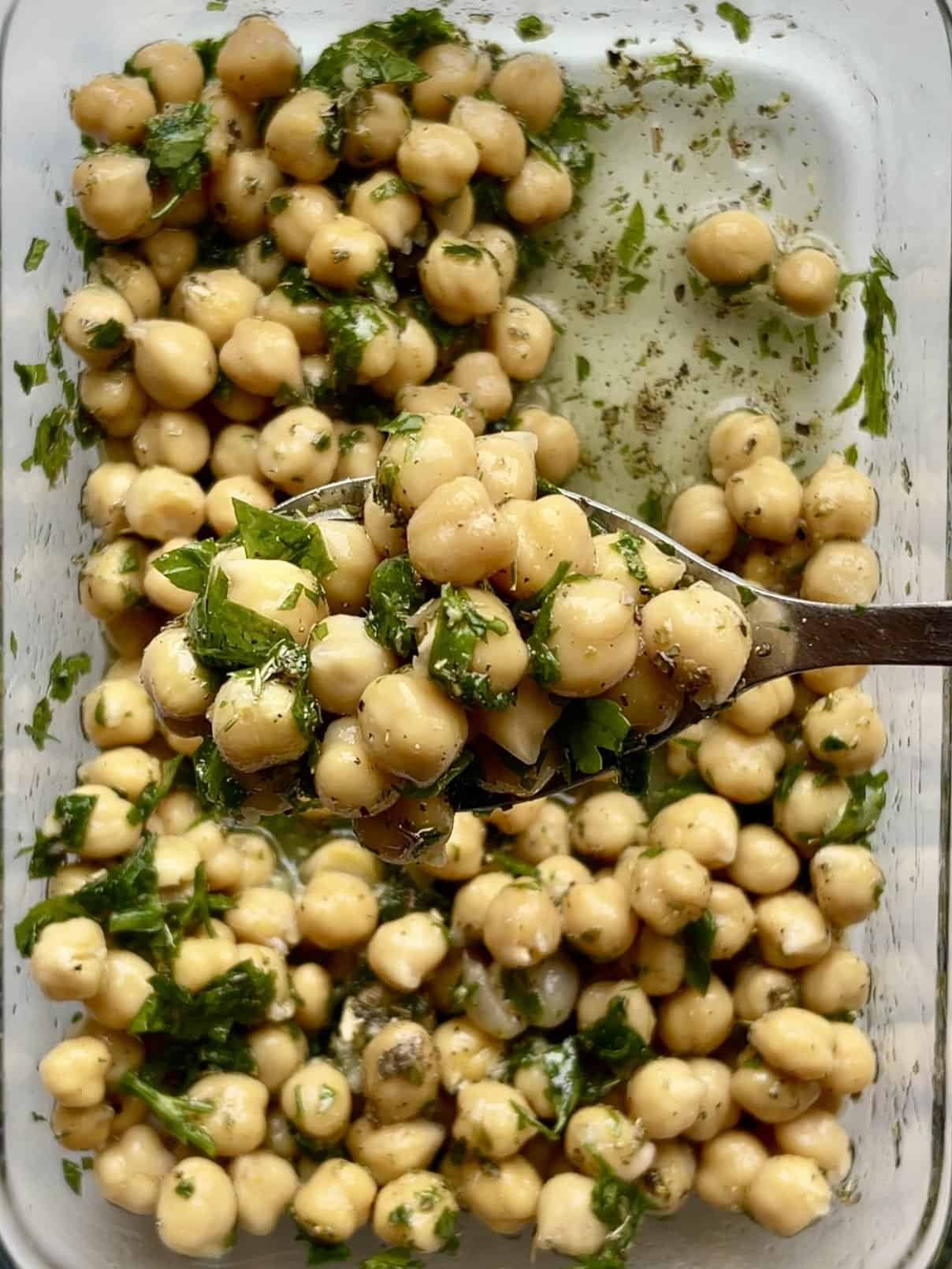 Soft, marinated chickpeas with herbs in a glass dish, ready to serve.