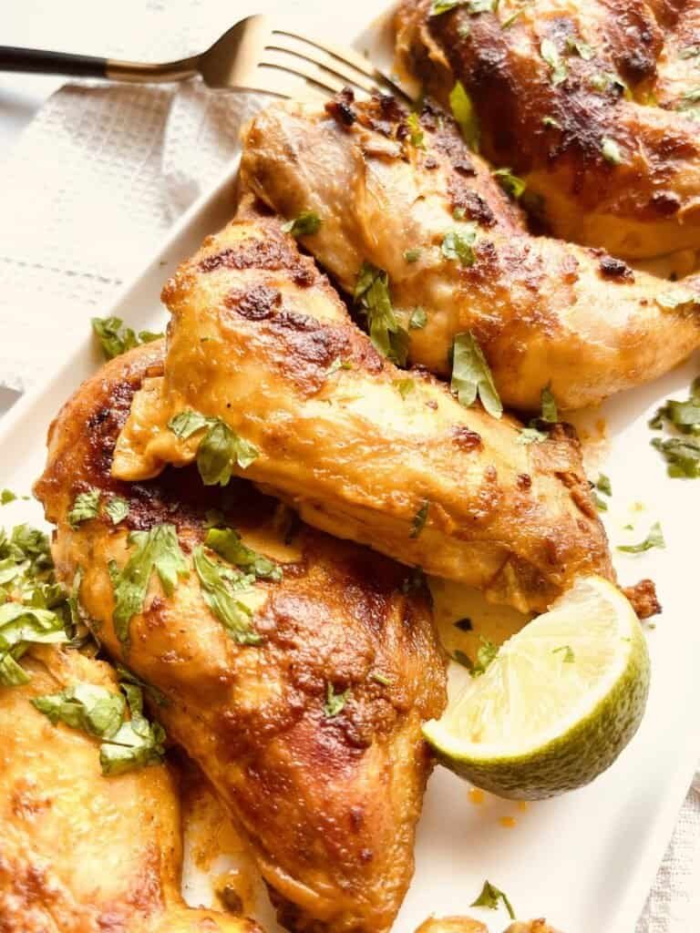 Grilled yogurt-marinated chicken drumsticks with fresh herbs and lime wedge on a white plate.