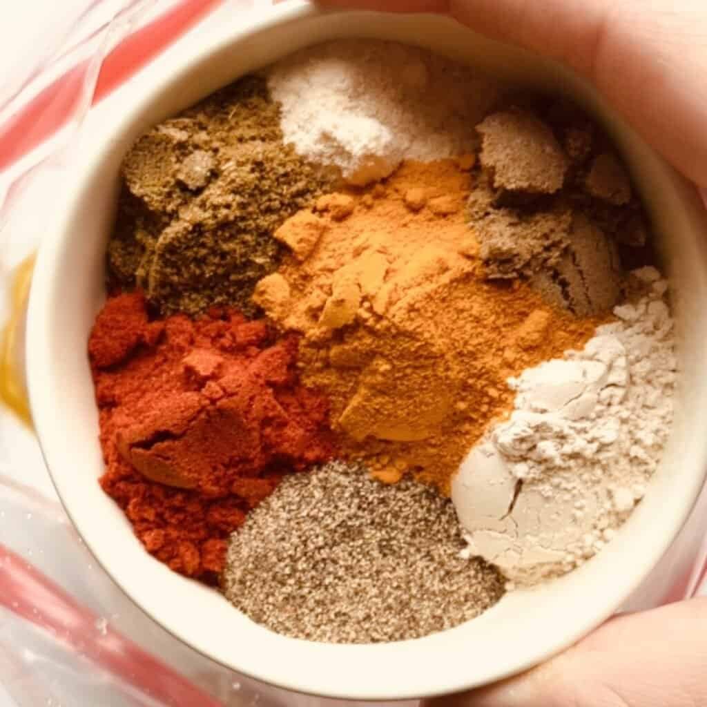 A vibrant mix of spices for Middle Eastern yogurt chicken marinade in a white bowl.