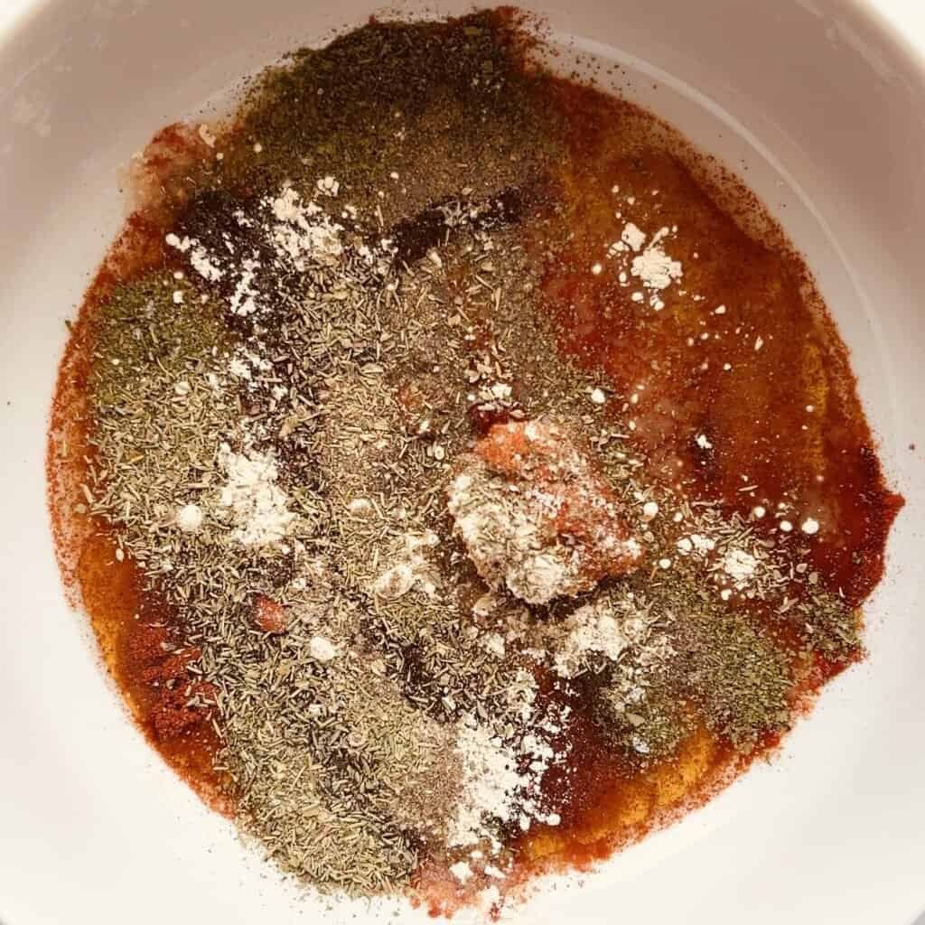 Paprika chicken marinade with spices and herbs in a white bowl.