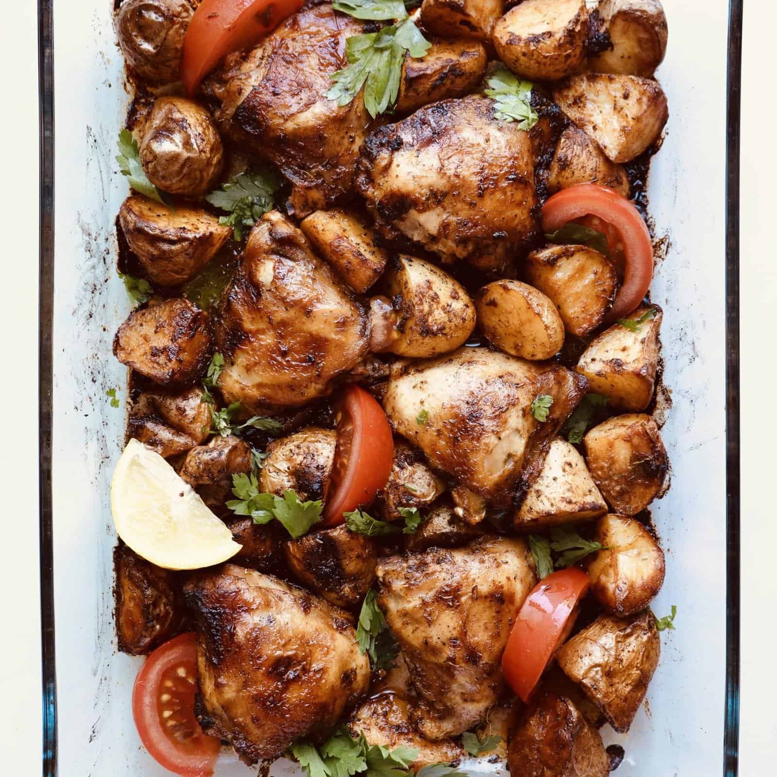 Grilled paprika chicken with roasted potatoes, cherry tomatoes, and fresh herbs on a baking dish. Pe.