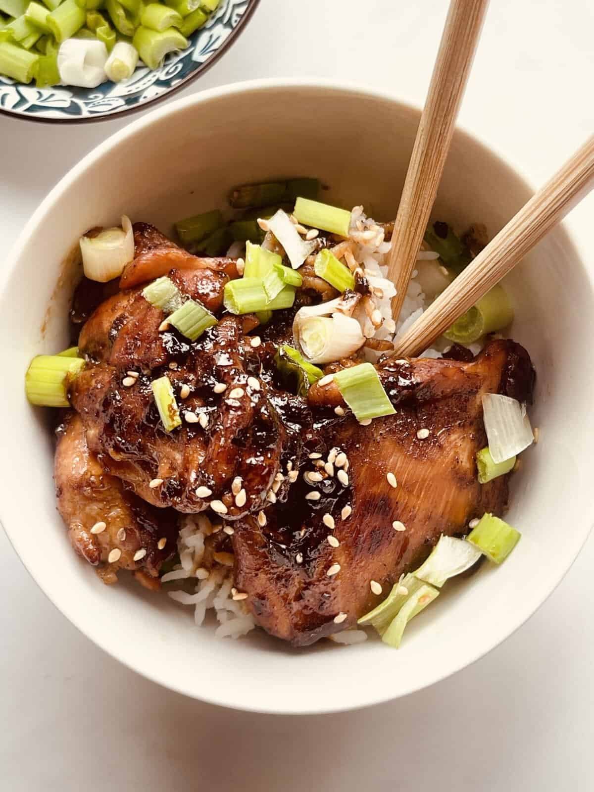 Grilled soy garlic chicken with green onions in a white bowl, garnished with sesame seeds.