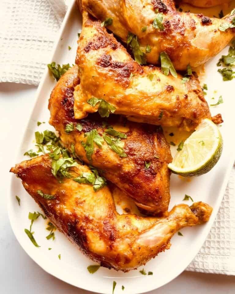 Grilled chicken drumsticks with herbs and lime wedge on white platter, close-up.