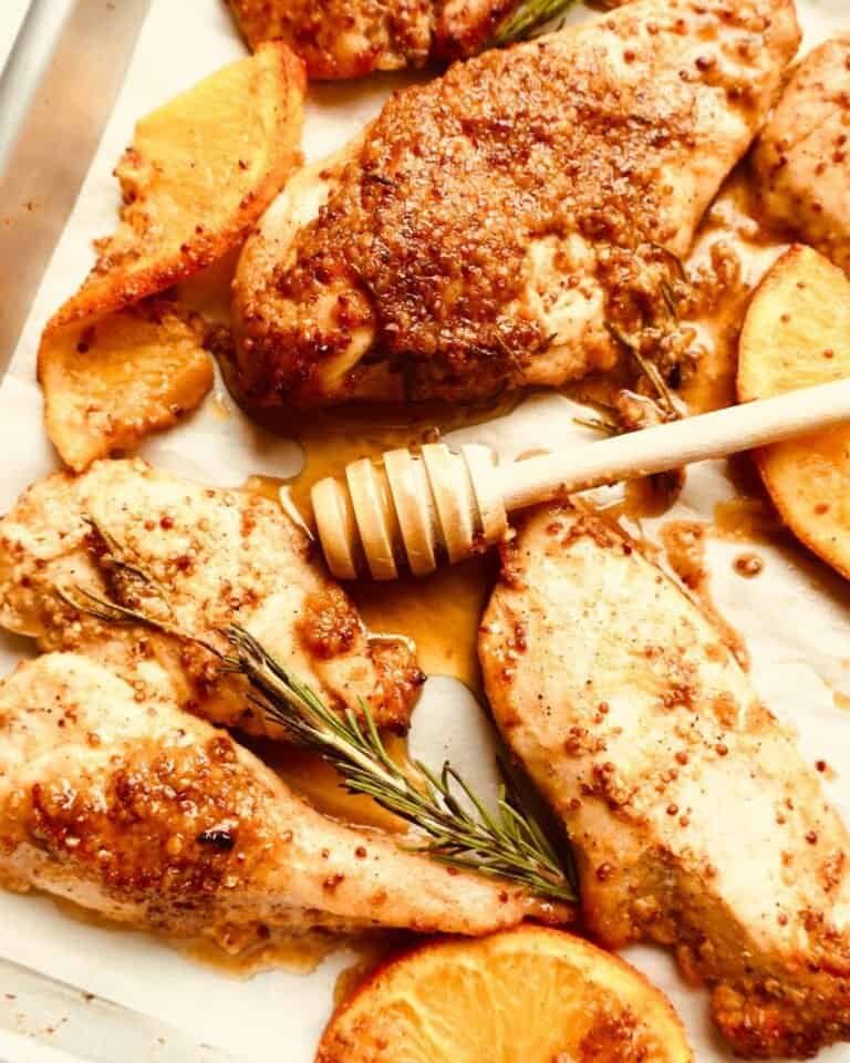 Golden baked chicken thighs with roasted potatoes and fresh rosemary on a baking sheet.