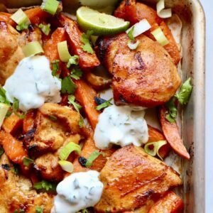 Grilled chicken thighs with roasted sweet potatoes, fresh lime, and creamy herb sauce on a baking sh.