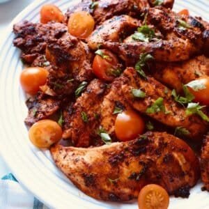 Grilled chicken wings with cherry tomatoes and fresh herbs on a white plate.