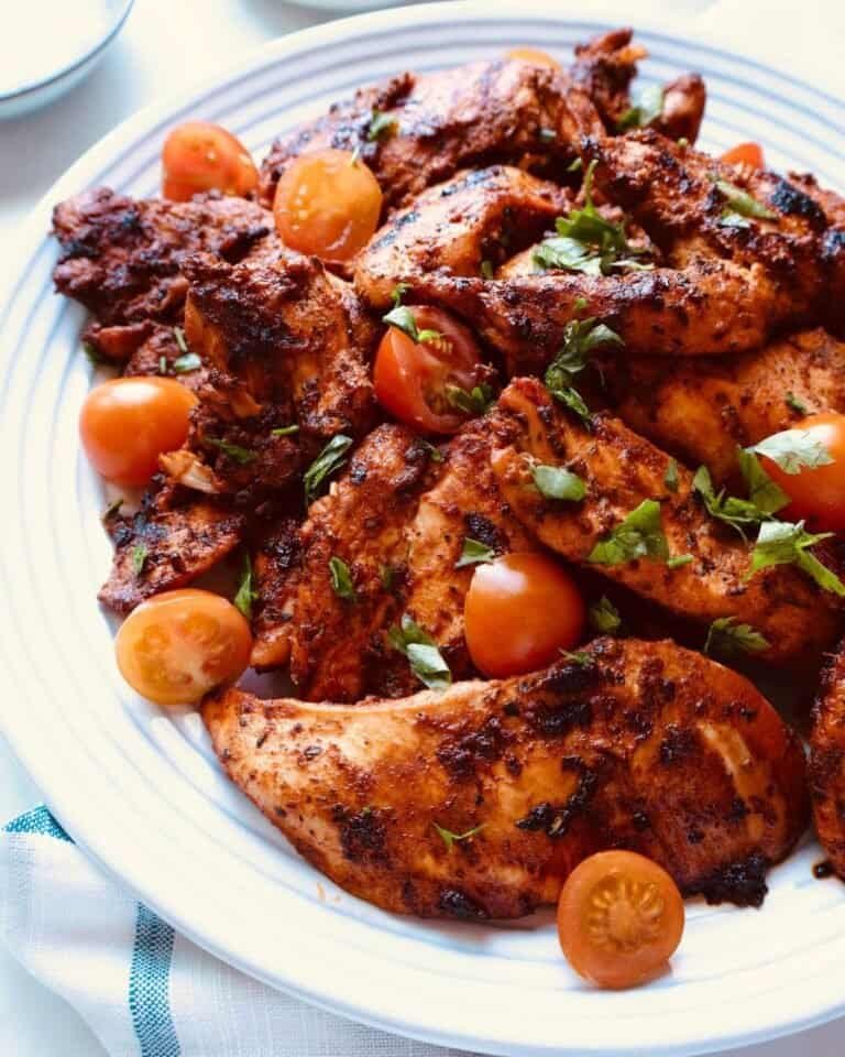 Grilled chicken wings with cherry tomatoes and fresh herbs on a white plate.