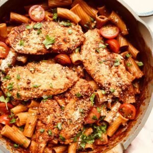 Grilled chicken thighs with pasta and cherry tomatoes in a skillet.