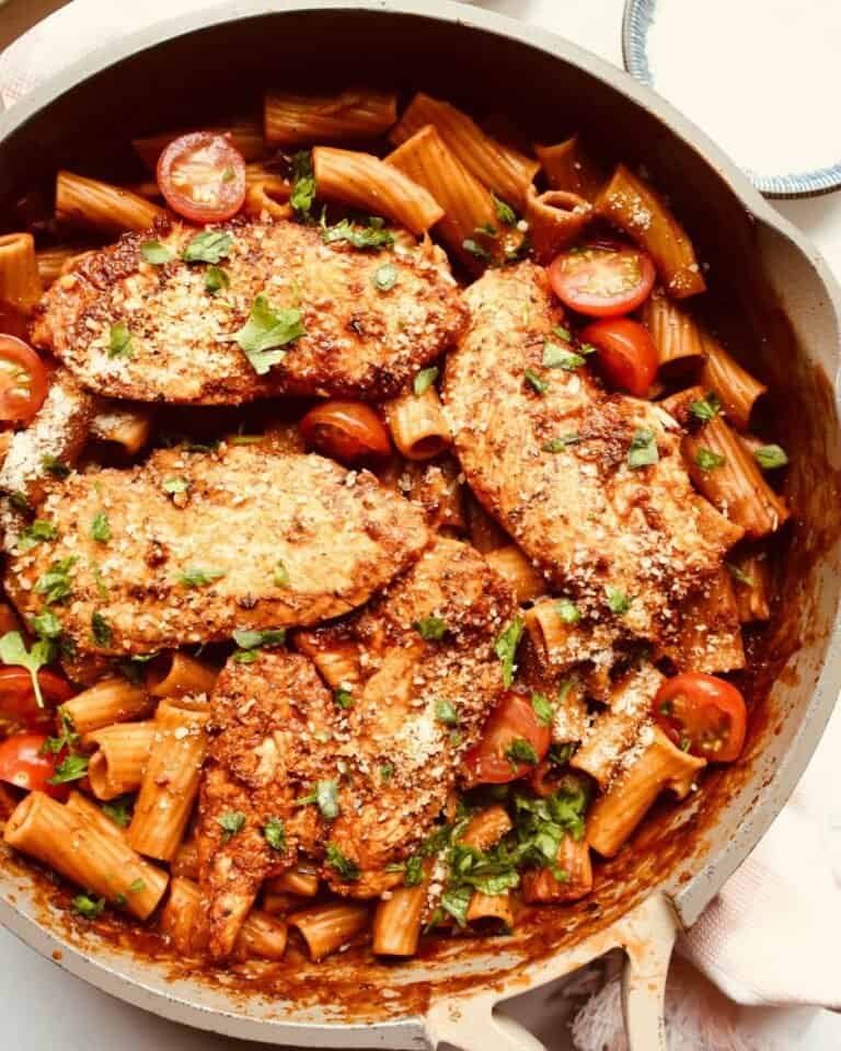 Grilled chicken thighs with pasta and cherry tomatoes in a skillet.