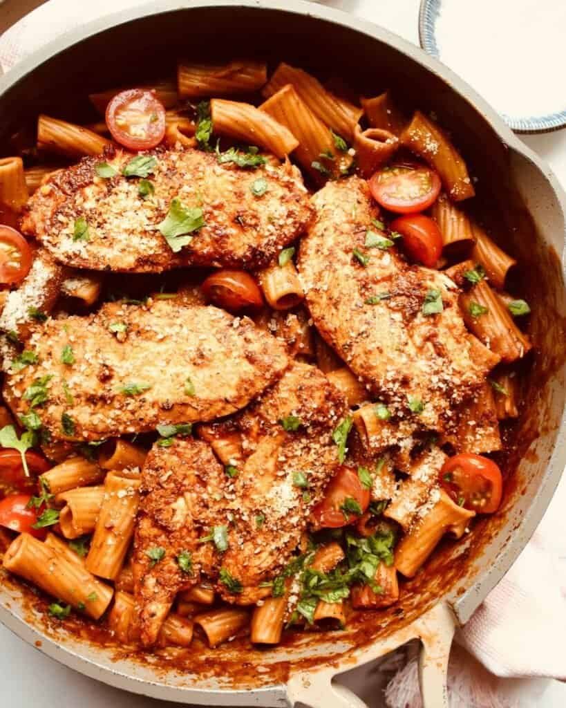 Grilled chicken thighs with pasta and cherry tomatoes in a skillet.