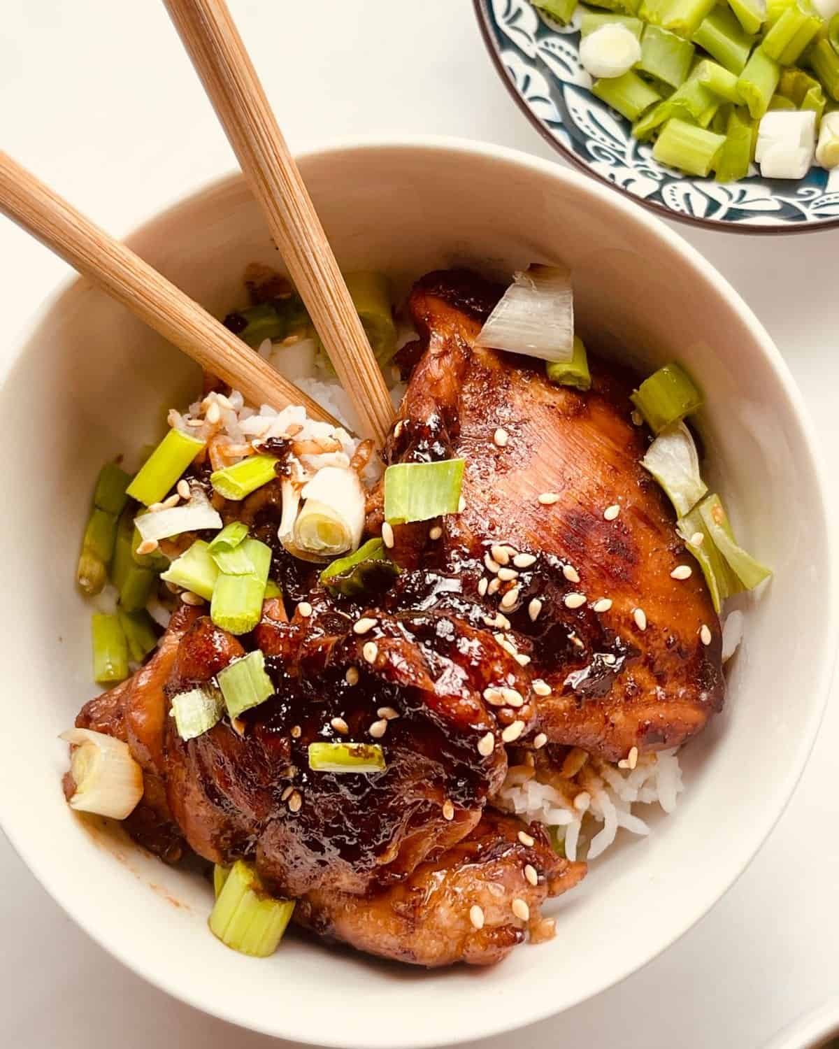 Succulent glazed chicken thighs with green onions served over rice in a white bowl.