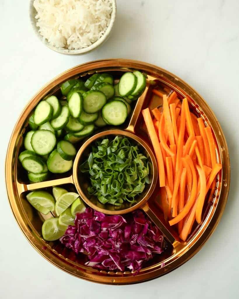 Fresh cucumber, carrot, red cabbage, and green onion slices in a round serving tray for Korean Beef Rice Bowl
