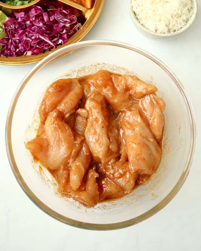 Grilled chicken marinated in chili honey sauce in a glass bowl for recipe preparation.