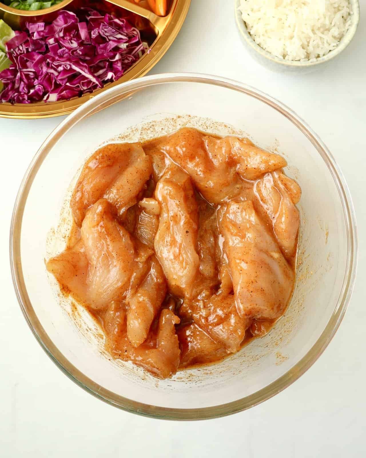 Grilled chicken marinated in chili honey sauce in a glass bowl for recipe preparation.