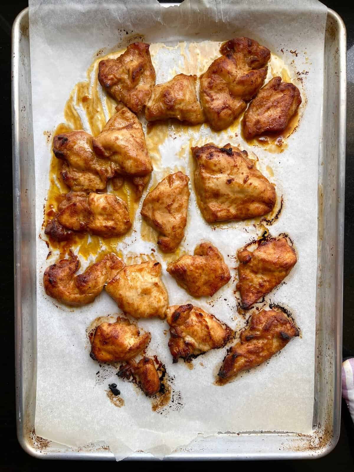 Grilled chili honey chicken pieces on a baking sheet with caramelized glaze.