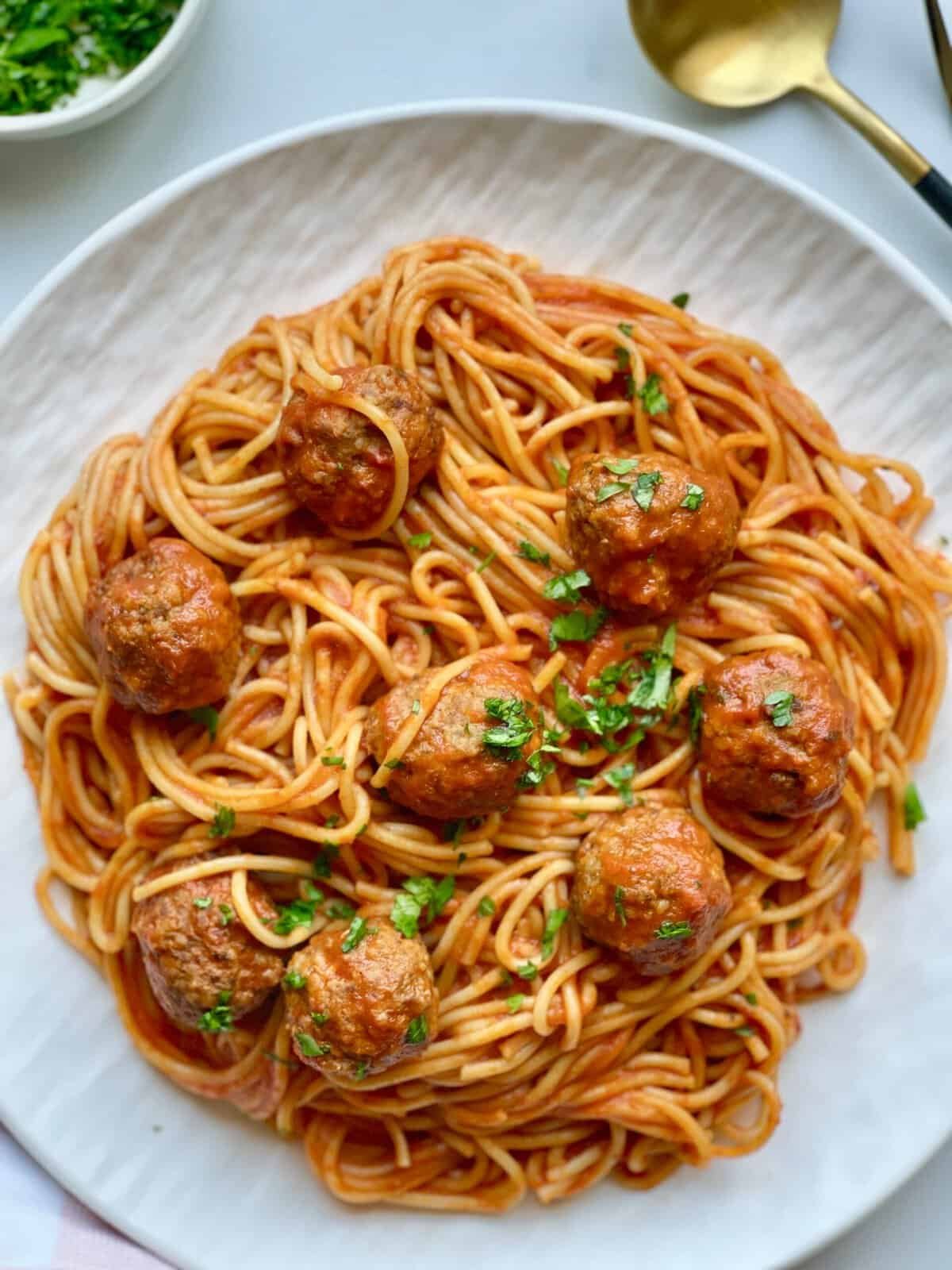 Delicious spaghetti with meatballs on a white plate, garnished with fresh herbs.
