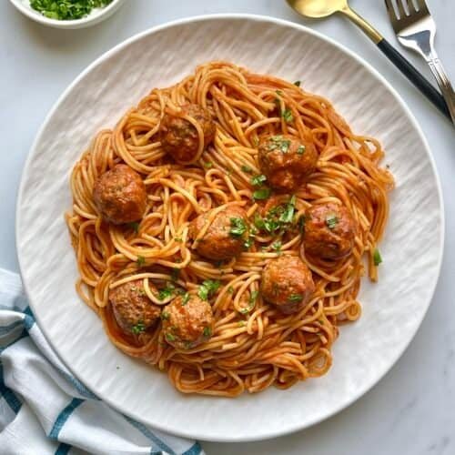 Creamy spaghetti with meatballs on a white plate, garnished with fresh herbs. Perfect comfort food f.