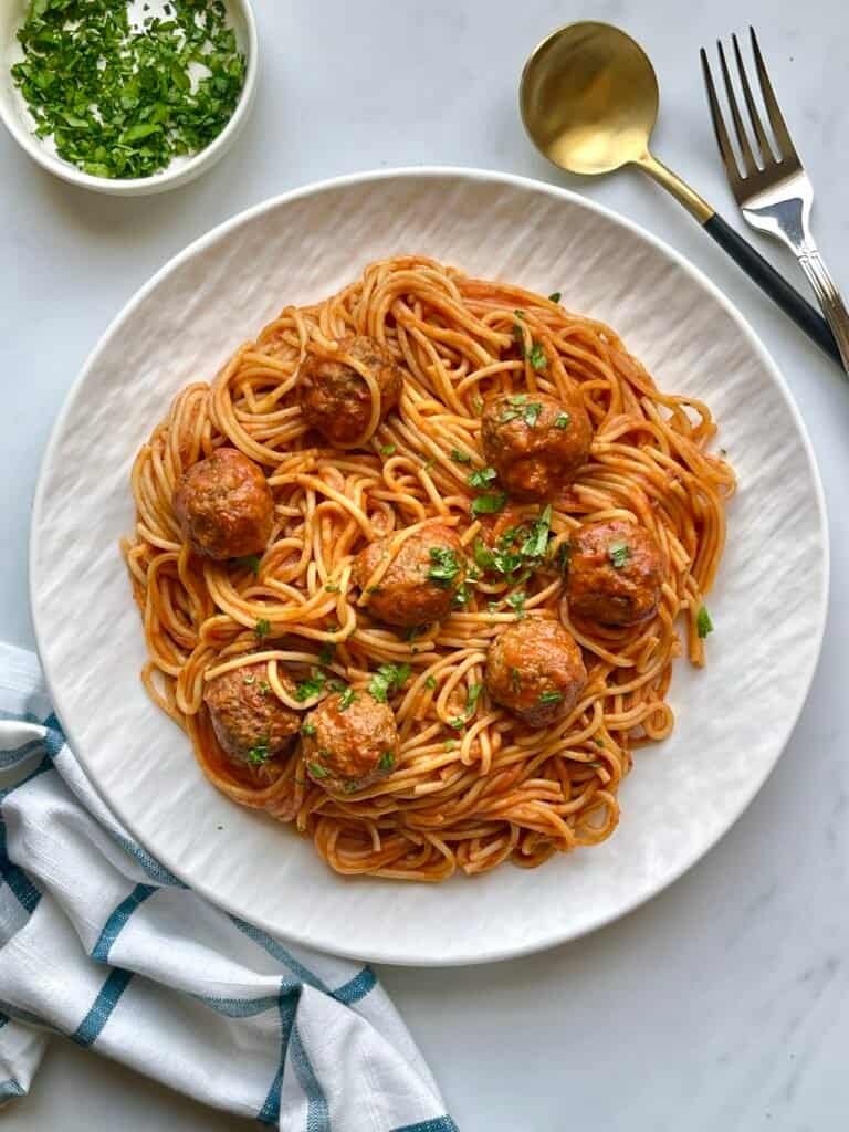 Creamy spaghetti with meatballs on a white plate, garnished with fresh herbs. Perfect comfort food f.