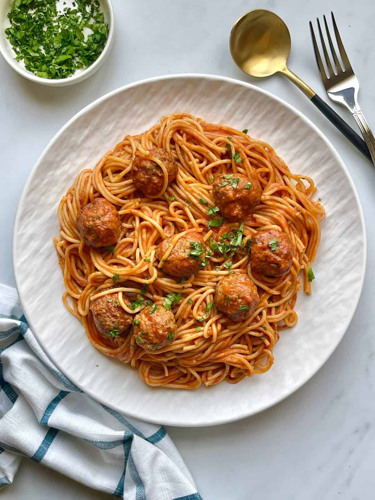 Creamy spaghetti with meatballs on a white plate, garnished with fresh herbs. Perfect comfort food f.