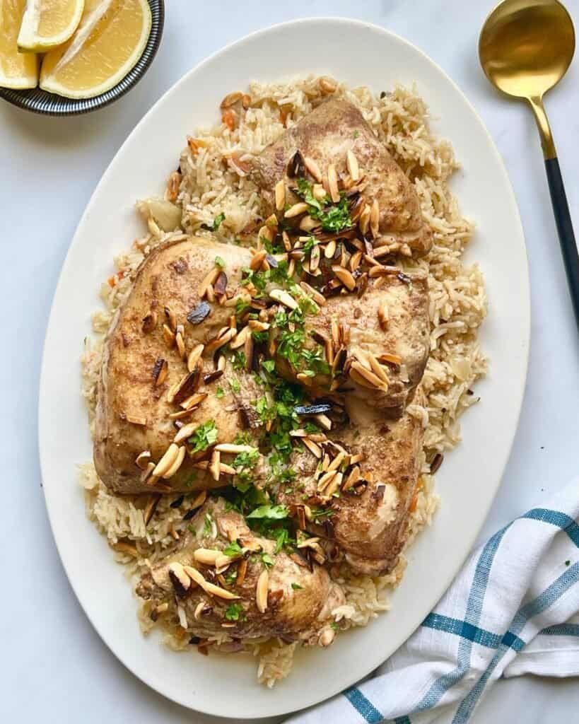 Succulent chicken thighs with almond topping served over fluffy rice on a white platter.