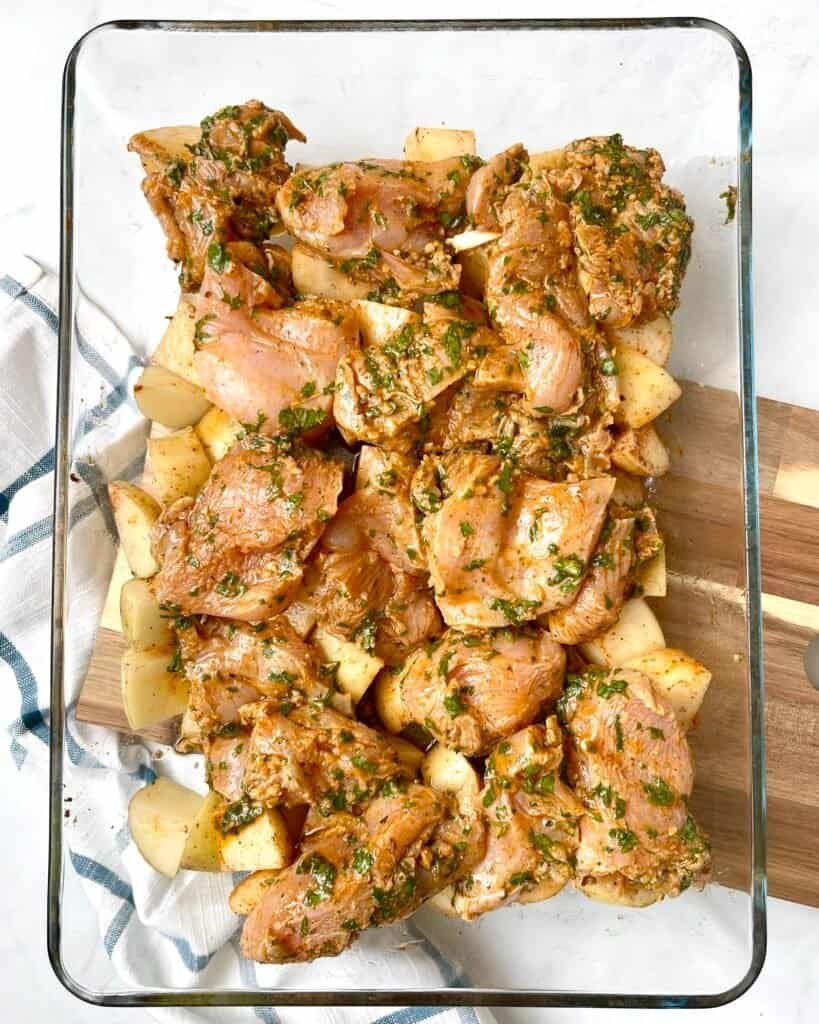 Marinated Mediterranean chicken layered on top of seasoned potatoes, ready for baking in this easy dump and bake chicken and potatoes one-pan dinner.
