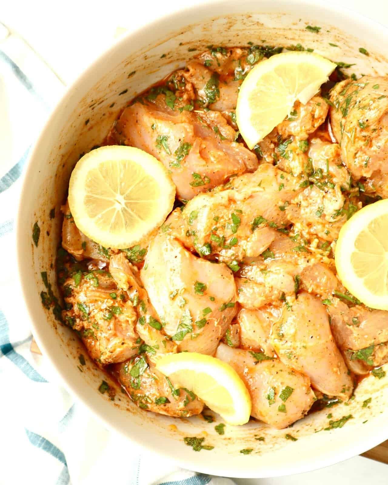 Mediterranean Herb Chicken Marinade in a white bowl with lemon slices.