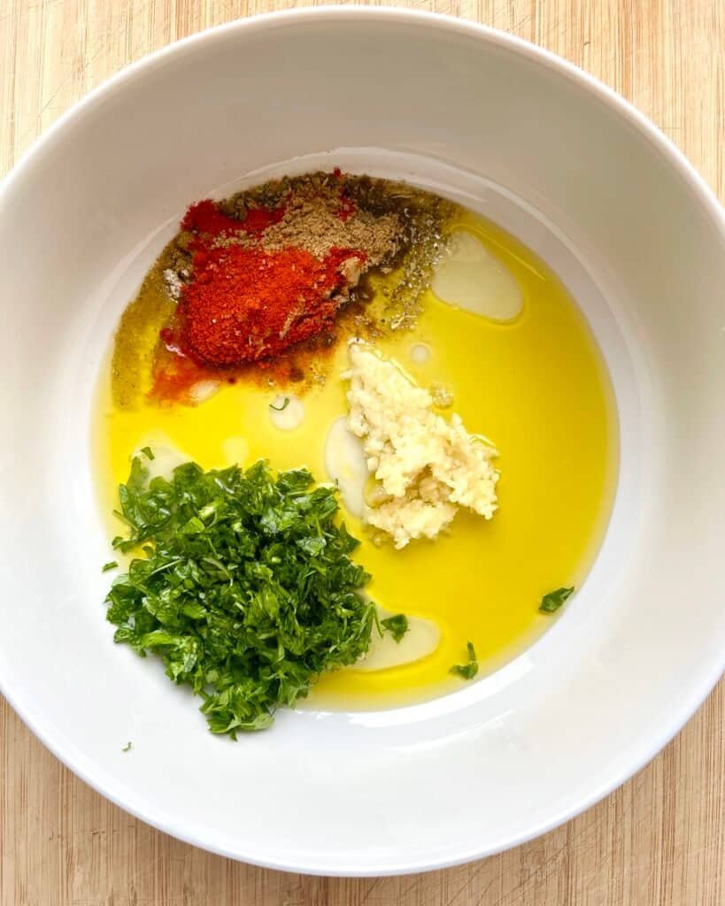 Adding Mediterranean Herb Chicken Marinade ingredients in a white glass bowl