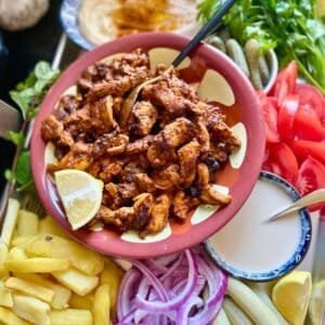 Grilled chicken shawarma served with fresh vegetables and creamy sauce on a colorful platter.