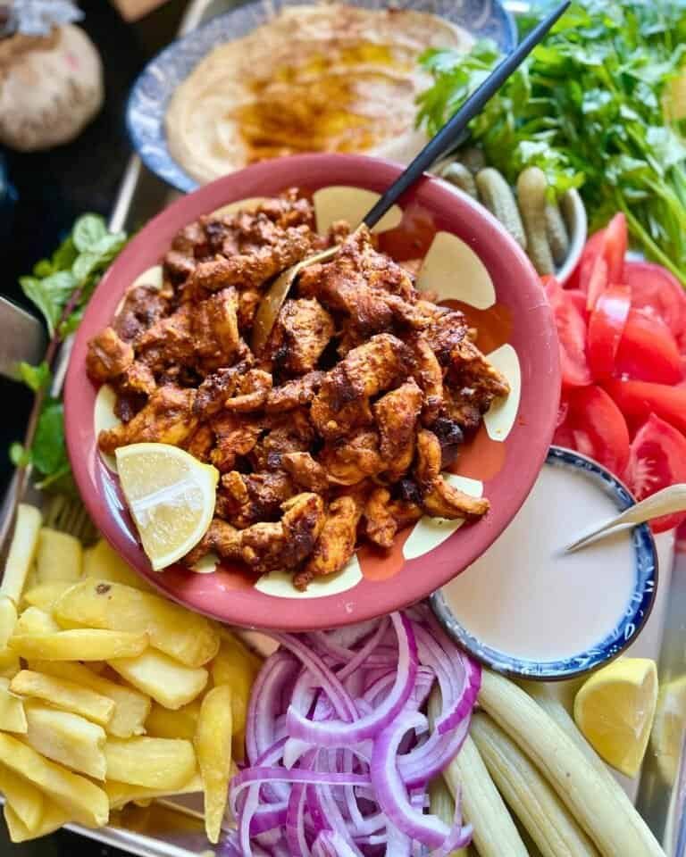 Grilled chicken shawarma served with fresh vegetables and creamy sauce on a colorful platter.