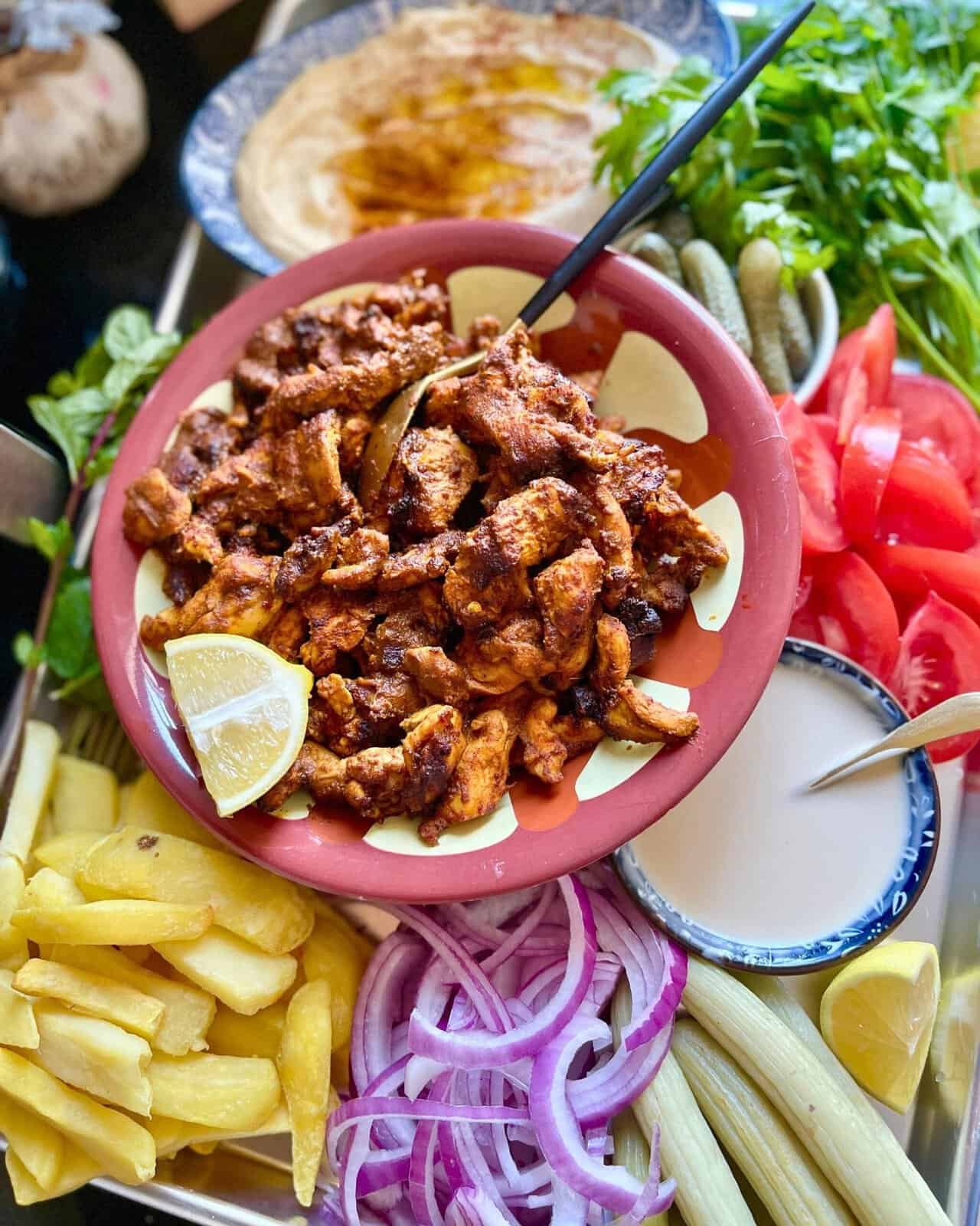 Grilled chicken shawarma served with fresh vegetables and creamy sauce on a colorful platter.