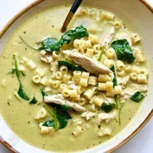 Creamy chicken pesto soup with pasta and spinach in a bowl, ready to serve.