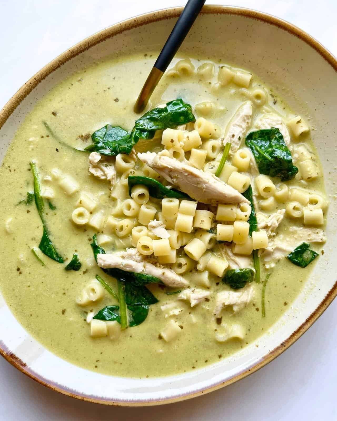 Creamy chicken pesto soup with pasta and spinach in a bowl, ready to serve.